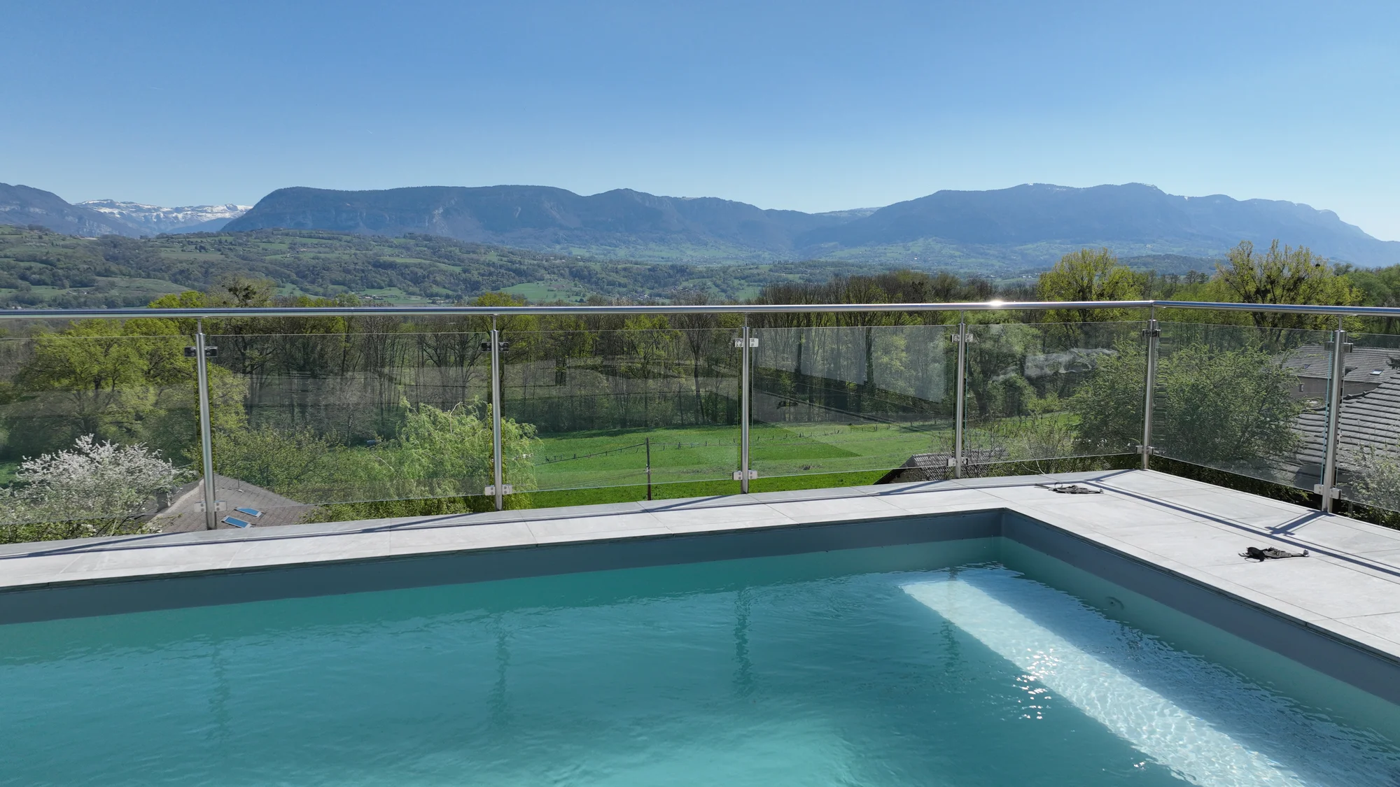 Garde-corps verre sur poteaux inox autour d'une piscine vue montagne · réalisation Erminox